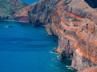 Yüksek çizgili uçurumlar, Portekiz 'in Madeira kentindeki Ponta de Sao Lourenco' da mavi Atlantik 'le buluşuyor. Açık gün ışığı pas kırmızısı, toprak rengi, kömür tabakası ve yatay lav akışını ortaya çıkarır..