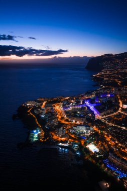 Teraslı yamaçlar Atlantik 'e iniyor. Kıvrımlı bir körfez altın ışıklarla parlıyor ve yüksek bir açıyla alacakaranlıkta yakalanan Madeira, Funchal' da canlı mavi aksanlar var..