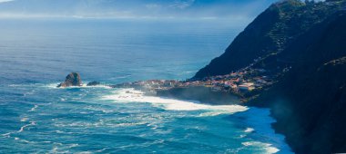Hava kıyı manzarası, Porto Moniz ve Seixal yakınlarındaki Madeira 'da teraslı kayalıkların altındaki küçük bir kasabaya doğru kıvrılan Atlantik dalgalarını gösteriyor..