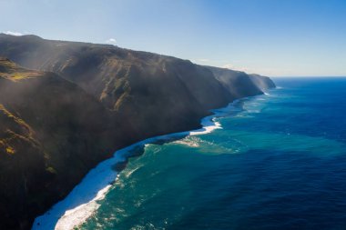 Dik volkanik kayalıklar Madeira 'daki Sao Vicente yakınlarındaki derin mavi Atlantik sularına dökülür, dalgalı bir kıyı boyunca beyaz dalgalar ve güneş ışığı terasları ve sisli gölgeleri ortaya çıkarır..