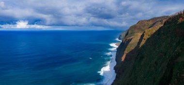 Madeira 'nın kuzeybatısının Veu da Noiva yakınlarındaki hava manzarası, yeşil uçurumlar Atlantik' e düşüyor, dar bir sahil çizgisi, alçak bulutlar sahne boyunca ışık saçıyor..