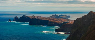 Ponta de Sao Lourenco, Madeira, Portekiz 'in hava gün ışığı manzarası, deniz yığınları ve pas kayalıkları ile volkanik burnu yumuşak bulutlar altında turkuaz suyu karşılıyor.