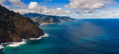 Hava görüntüsü Madeira 'nın kuzey kıyısı bazalt kayalıkları ve Seixal ve Sao Vicente yakınlarında kümülüs gölgeleri, canlı okyanus renkleri ve parlak gün ışığında tepeleri olduğunu gösteriyor..