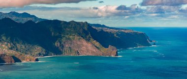 Katmanlı bazalt kayalıkları Ponta de Sao Lourenco yakınlarındaki Atlantik 'e iniyor, engebeli burunlar, koylar ve teras köyleri yumuşak öğleden sonra ışığı ve bulutları altında..