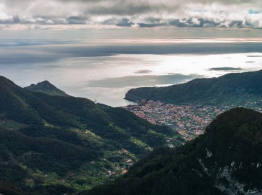 Yüksek görüş açısı yeşil dağların üzerinden Sao Vicente, Madeira, Portekiz 'e bakar. Alçak bulutlar ayrılıyor ve ışık Atlantik 'e ve yamaçlara gümüş döküyor..