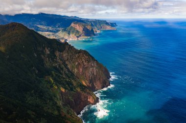 Hava görüntüsü, Ponta de Sao Lourenco yakınlarındaki Madeira kuzey kıyısında volkanik kayalıklar, teraslı yamaçlar ve promontuarları gösteriyor. Gün ışığı, sis ve turkuaz su üzerinde sörf..