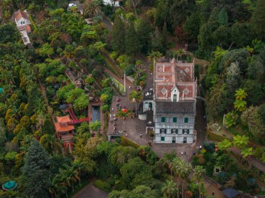 Hava görüntüsünde Monte Sarayı, kırmızı kiremitli çatılar, göletler, yollar ve Madeira Funchal 'da kırmızı bir pavyon görünüyor. Ziyaretçiler güpegündüz teraslarda ve meydanda toplanıyor..