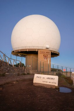 Pico do Arieiro, Madeira 'da kartal amblemi, çit ve dikenli telle dolu bir Forca Aerea üssü üzerinde sıcak, alçak ışık ve temiz gökyüzünde beyaz bir jeodezik radar kubbesi yükselir..