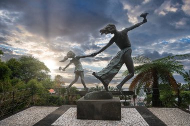 Bronz kadın ve çocuk Portekiz, Funchal, Madeira 'daki Jardim Monte Sarayı' nda taş bir kaide üzerinde dans ediyorlar. Kadın gün batımında bir kuşu kaldırıyor..