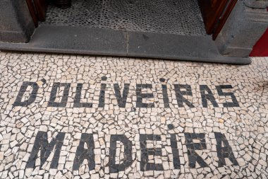 Calcada Mozaik büyüleri, Funchal 'daki bir binanın girişinde D' Oliveiras Madeira 'yı koyu bazalt eşiği ve ahşap kapıları eşit ışıklandırılmış ve sıkıca çerçevelenmiş bir şekilde kapatır..