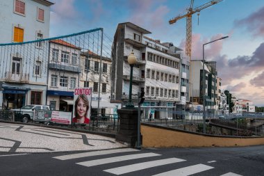 Funchal, Madeira, akşam sokak gösterileri fayanslı gezinti güvertesi ve yaya geçidi, sarı bir vinç, tatil çelenkleri, ve mağaza ve balkonların yakınında bir CONTIGO kampanya posteri.