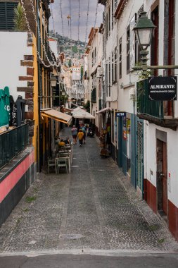 Funchal, Madeira, Portekiz 'de dar bir kaldırım taşı yolu beyazlatılmış cepheleri, yeşil panjurları, festival ışıklarını, kafe masalarını, ALMIRANTE tabelasını, ATM' yi ve yemek yiyen insanları gösteriyor..