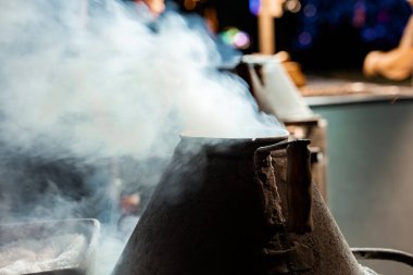 Funchal, Madeira 'daki konik bir metal kazandan yükselen buhar. Kaba bir kulp ve kenar, koyu bokeh, sade anahtar aydınlatma ve sığ alan derinliği ile sıcak bir ışık yakar..