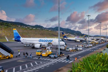 Funchal 'daki Cristiano Ronaldo Madeira Uluslararası Havalimanı' nda yer ekipleri Ryanair ve Discover uçakları, dik teraslı tepelerin ardında bir akşam gökyüzü altında yürürken,.