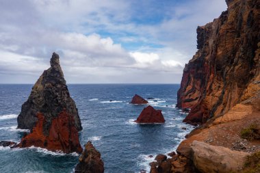 Portekiz, Madeira 'daki Ponta de Sao Lourenco' daki pas kırmızısı kayalıkların yanında dalgalı deniz yığınları yükselir. Rüzgâr süpürdü dalgalar bazalt vurdu ve demir zengini katmanlar kasvetli bir gökyüzünün altında.
