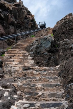 Engebeli bir taş merdiven, karanlık bazalt boyunca Madeira, Ponta de Sao Lourenco 'da hafif bulutlu bir ışık altında dar bir demiryolu hattına doğru tırmanıyor..