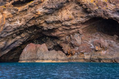 Katmanlı bazalt ve pas tüyü, Ponta de Sao Lourenco yakınlarındaki Madeira 'da tırtıklı kemer ve küçük mağaralar oluşturur. Yumuşak gün ışığı, sakin turkuaz su üzerindeki çizgileri ortaya çıkarır..