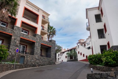 Funchal, Portekiz 'de sessiz bir yokuş yukarı, kırmızı çizgili beyaz cepheler, lav taşı temelleri, kiremitli çatılar, balkonlar, palmiye ağaçları ve bulutlu gökyüzü altında park yasağı işareti arasında kıvrımlar..