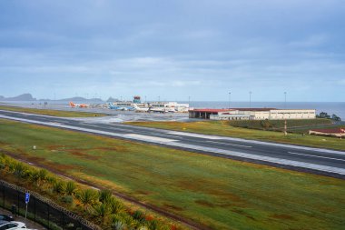 Madeira Adası 'ndaki Funchal Havalimanı' nın zemin katı, jetler terminalden kuleye, pistler Atlantik 'e paralel, rutubetli asfalt, bulutlu ışık, engebeli adalar görünür..