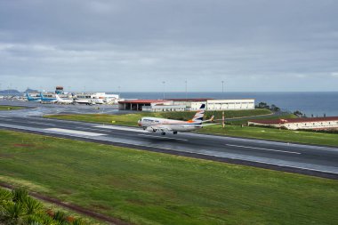 Bir yolcu uçağı Funchal yakınlarındaki Cristiano Ronaldo Madeira Havaalanına iniyor. Atlantik Okyanusu, terminaller, hangarlar ve kontrol kulesi bulutlu ışık altında kalır..