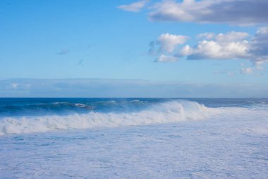 Portekiz, Madeira 'da kümülüs bulutlarının altında Atlantik dalgaları çarpar ve köpürür. Doğal gün ışığı, uzun yatay bileşim, sisli sprey ve geniş ufuklar..