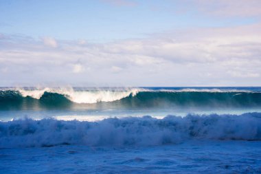 Turkuaz Atlantik dalgaları Madeira, Portekiz 'e doğru sisli bir sprey ve kırılan bir duvarla, berrak gün ışığı, katmanlı bulutlar, durgun soluk gökyüzü, doku ve hareket.
