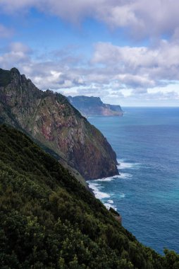 Portekiz 'in Madeira şehrinde, Ponta de Sao Lourenco yakınlarındaki yeşil bitki örtüsü ile sarp deniz kayalıkları kırılmış bulutların altında kayalara çarpıyor..