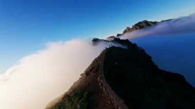 Portekiz 'in Madeira adasında gün batımında Pico do Arieiro' da bulutların üzerinde uçmak. Bulutların üstünde sihirli günbatımı manzarası dağ sıraları ve yürüyüşçülerin yanında uçuyor..