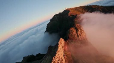 Portekiz 'in Madeira adasında gün batımında Pico do Arieiro' da bulutların üzerinde uçmak. Bulutların üstünde sihirli günbatımı manzarası dağ sıraları ve yürüyüşçülerin yanında uçuyor..