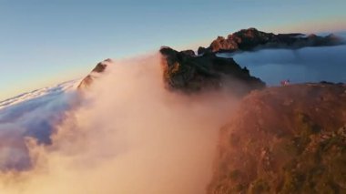 Portekiz 'in Madeira adasında gün batımında Pico do Arieiro' da bulutların üzerinde uçmak. Bulutların üstünde sihirli günbatımı manzarası dağ sıraları ve yürüyüşçülerin yanında uçuyor..