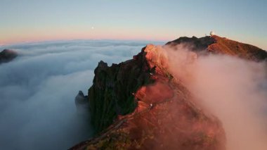 Portekiz 'in Madeira adasında gün batımında Pico do Arieiro' da bulutların üzerinde uçmak. Bulutların üstünde sihirli günbatımı manzarası dağ sıraları ve yürüyüşçülerin yanında uçuyor..
