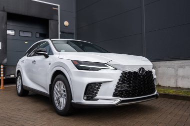 Beyaz Lexus RX 450 h + F SPORT karanlık panel duvarları ve yükleme alanında kaldırım kenarında oturur. Bulutlu ışık Milli ızgara, keskin LED farlar, alaşım tekerlekleri tanımlar.