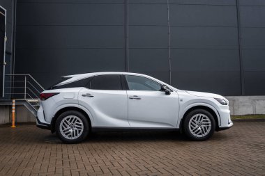 Beyaz Lexus RX 450h artı koyu metal kaplı endüstriyel bina ve merdivenlerin yanındaki tuğla parka park edilmiş F spor rozetleri, alaşımlı tekerlekler, keskin çizgiler ve bulutlu ışıkta melez tasarımı gösteriliyor..