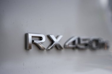 Yakından bakınca, krom RX RX 450h artı bir Lexus arka tarafında, RX diyez ve dağınık gün ışığında bulanıklaşan diğerleri, tanımlamada hibrit prizi vurguluyor..