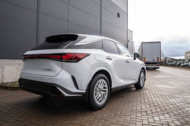 Beyaz Lexus RX 450 saat artı arka taraftan modern endüstriyel bir bina, LED stop lambası ve Lexus harfleri bulutlu ışıkta görünür..