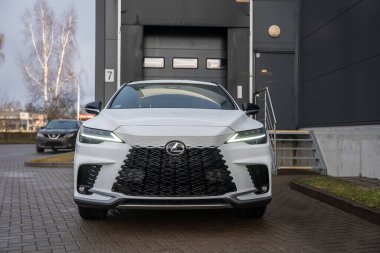 Beyaz bir Lexus RX 450 saat artı yükleme bölmesi kapısı ve metal merdivenlerin yanındaki asfalt bir garaj yolunda park edilmiş. Milli ızgara, L farları ve tampon girişleri merkezde..