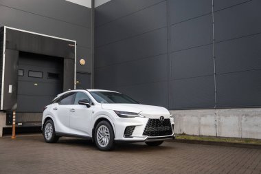 Beyaz Lexus RX 450 saat artı Milli ızgara ve LED ışıkları modern bir ticari parktaki Hormann rıhtımının yanında duruyor..