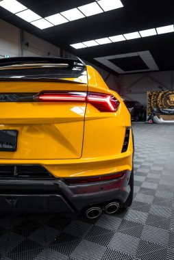 Üç çeyrek görünüm LED arka lamba, karbon fiber difüzyon, dörtlü egzozlar ve dama tahtası tabanı ve tavan lambası panelleri olan iyi aydınlatılmış bir garajda spoiler gösteriyor..