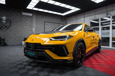 Sarı Lamborghini Urus Performante siyah ve kırmızı kareli bir garaj zemininde oturuyor. Düşük açı ise agresif ön, siyah tekerlekler, turuncu kalibreler ve karbon fiber aksanlar gösteriyor..