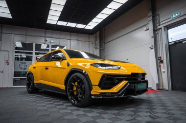 Alçak açı üç çeyrek görüntü, agresif bir ön, siyah çatı, karbon süsleme ve gri ışıklı gri kalibreli bir stüdyoda konuşan tekerlekleri gösteriyor..