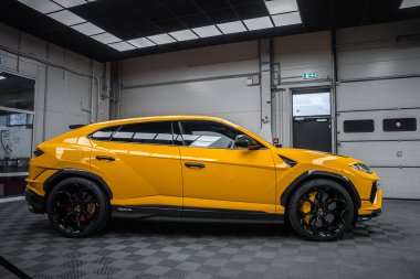 Parlak sarı Lamborghini Urus Performante modern bir bakım hangarında oturuyor. Siyah aero aksanları, sarı kalibreli büyük siyah tekerlekler, Y farları ve havalandırmalar göze çarpar..