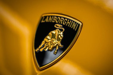Lamborghini tepesine yakın sarı bir panelde, altın boğa ve Lamborghini yazılı siyah bir kalkanın üzerinde sığ bir alan derinliği ile kontrollü aydınlatma..