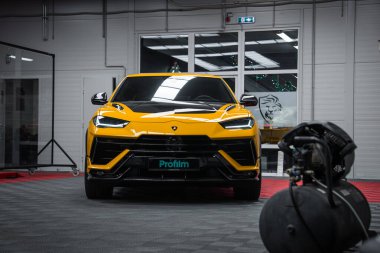 Parlak sarı Lamborghini Urus Performante bir Profilm garajında, LED farları, siyah aero aksanları, fayanslı zemini, cam bölümleri ve bir detay makinesi ile öne bakıyor..