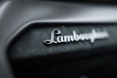 Yakından bakınca siyah desenli metalik Lamborghini amblemi görünüyor. Sığ alan derinliği ve karamsar ışıklandırma, lüks ve işçiliği çağrıştırıyor..