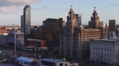 Liverpool üzerindeki hava gündoğumu Kraliyet Karaciğer Binası, Liverpool Müzesi ve cam kuleleri gösteriyor. Yavaş bir insansız hava aracı, rıhtım çadırlarını, araçları ve yayaları ortaya çıkarıyor..