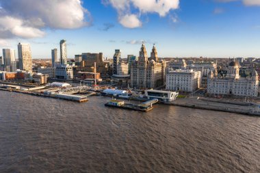 Mersey Nehri 'ndeki Liverpool rıhtımının hava gündoğumu manzarası. Üç Zarafet, Liverpool Müzesi, rıhtım ve feribot terminalleri sıcak ışık ve uzun gölgelerde görünür..