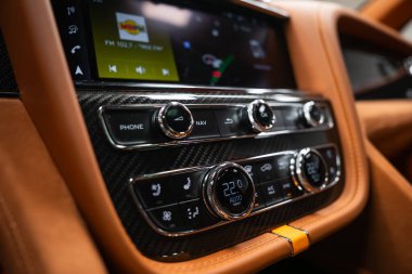 Yakından bakınca karbon fiber kaplama, düğümlenmiş kadranlar, ten rengi deri ve kontrastlı dikişler görünüyor. Ekranda telsiz ve navigasyon görünüyor. İklim 22 C ve koltuk ısıtıcısı..