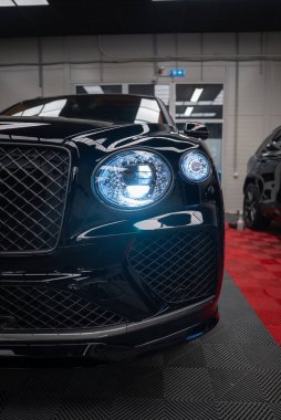 Kapalı alanda siyah Bentley Bentayga Speed 'in üç çeyrek görüntüsünü kapatın. Kristal kesimli LED farlar parıldıyor, matris ızgarası ve giriş göstergesi, kırmızı ve siyah zemin ve beyaz duvarlar mevcut.