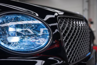 Mavi LED far ve elmas ızgara ızgara, parlak yansımalar ve sığ alan derinliği ile kapalı bir galeride siyah Bentley Bentayga Speed yakın çekim.