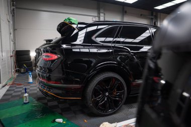 Parlak siyah Bentley Bentayga Speed kapalı bir bölmede oturuyor. Bagaj kapağı açık, mikro fiber havlular perdeler, oval stop lambaları ve ince çizgili gösteriler şebeke ışıkları altında..